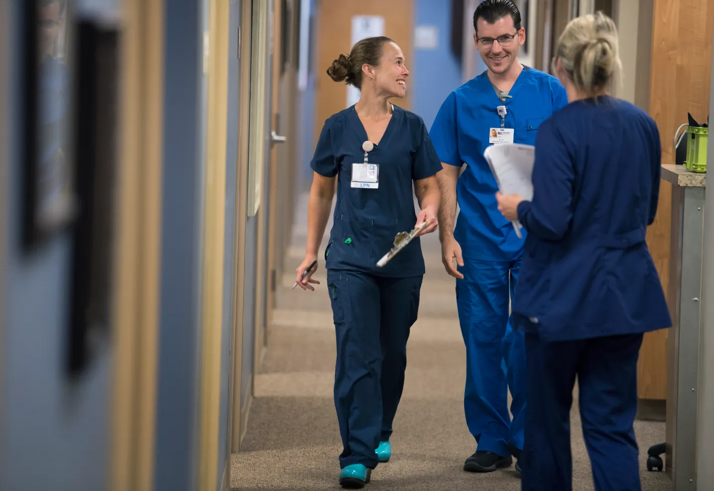 Three team members smiling while walking down a clinic hallway. Three team members smiling while walking down a clinic hallway.