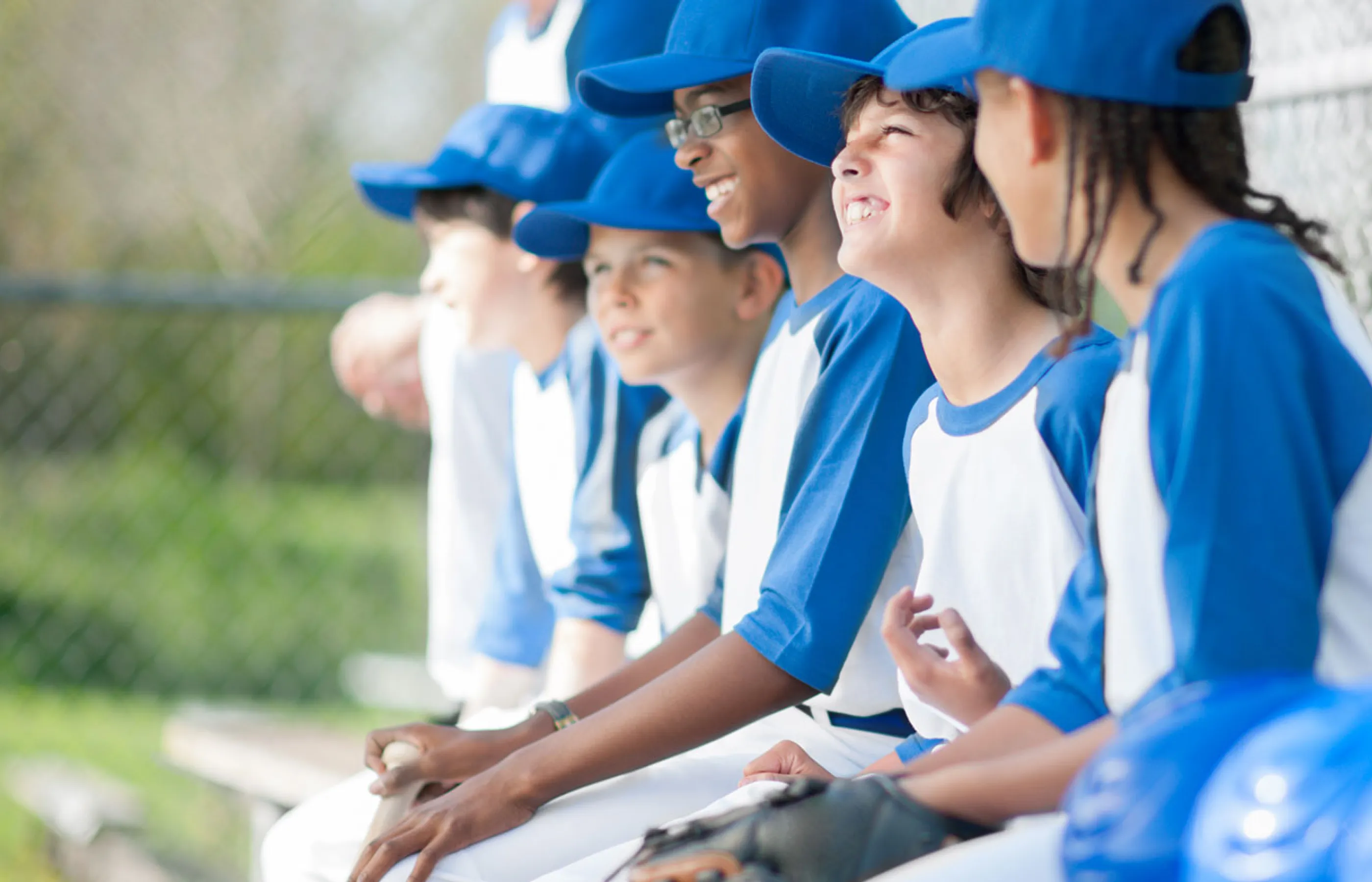 A team of young baseball players are sitting on a bench talking and laughing together