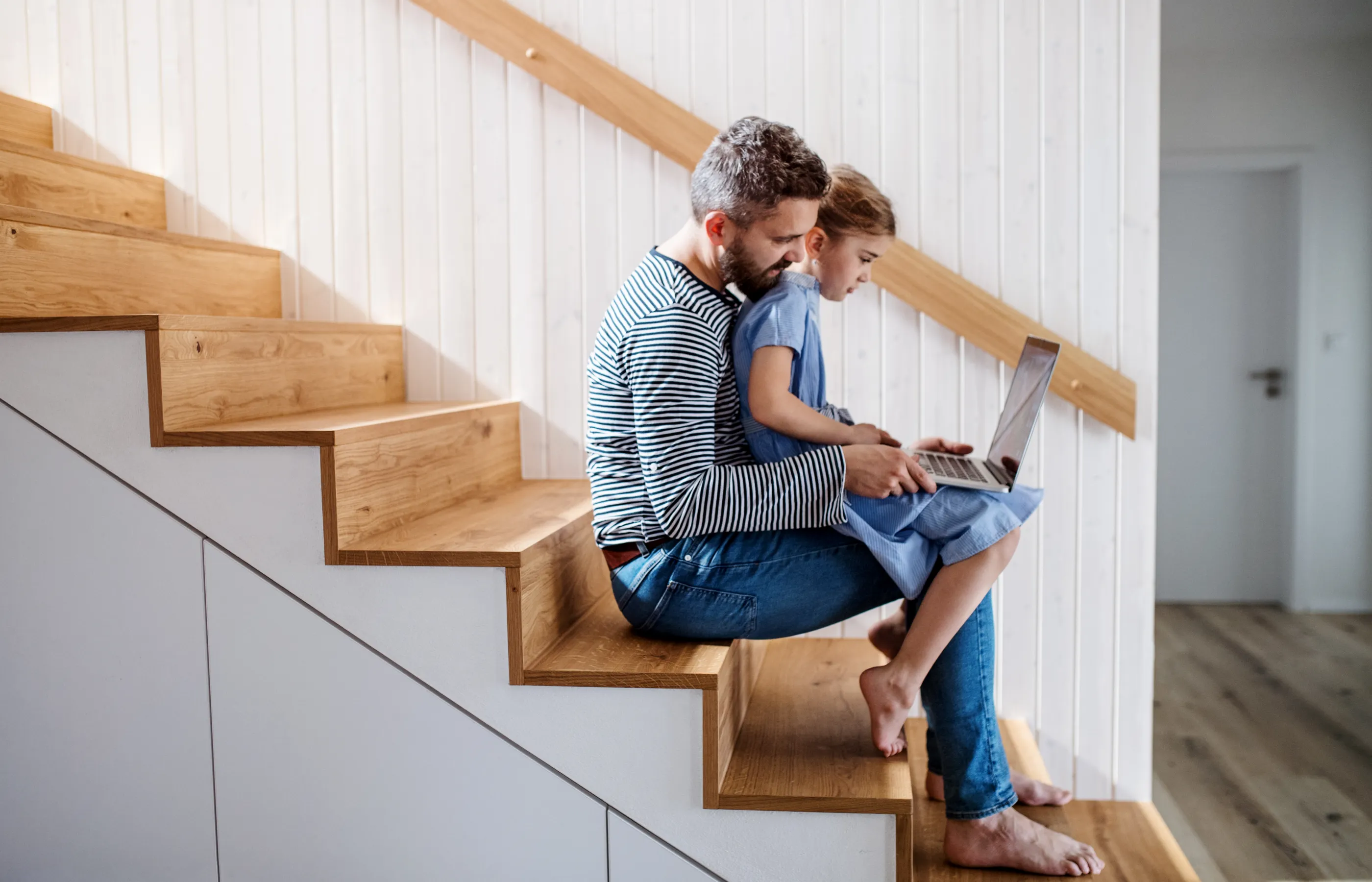 Father sitting with child on their home staircase looking at a laptop computer. 