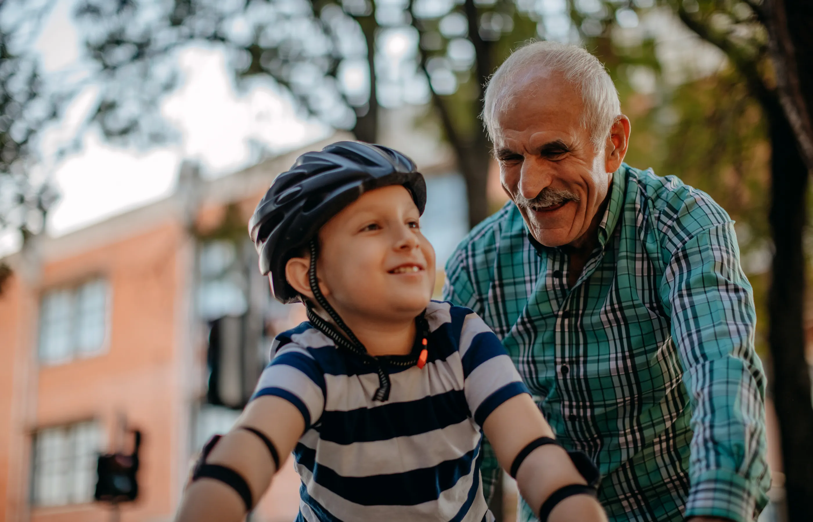 An older man is assisting his grandson as he rides his bike. 