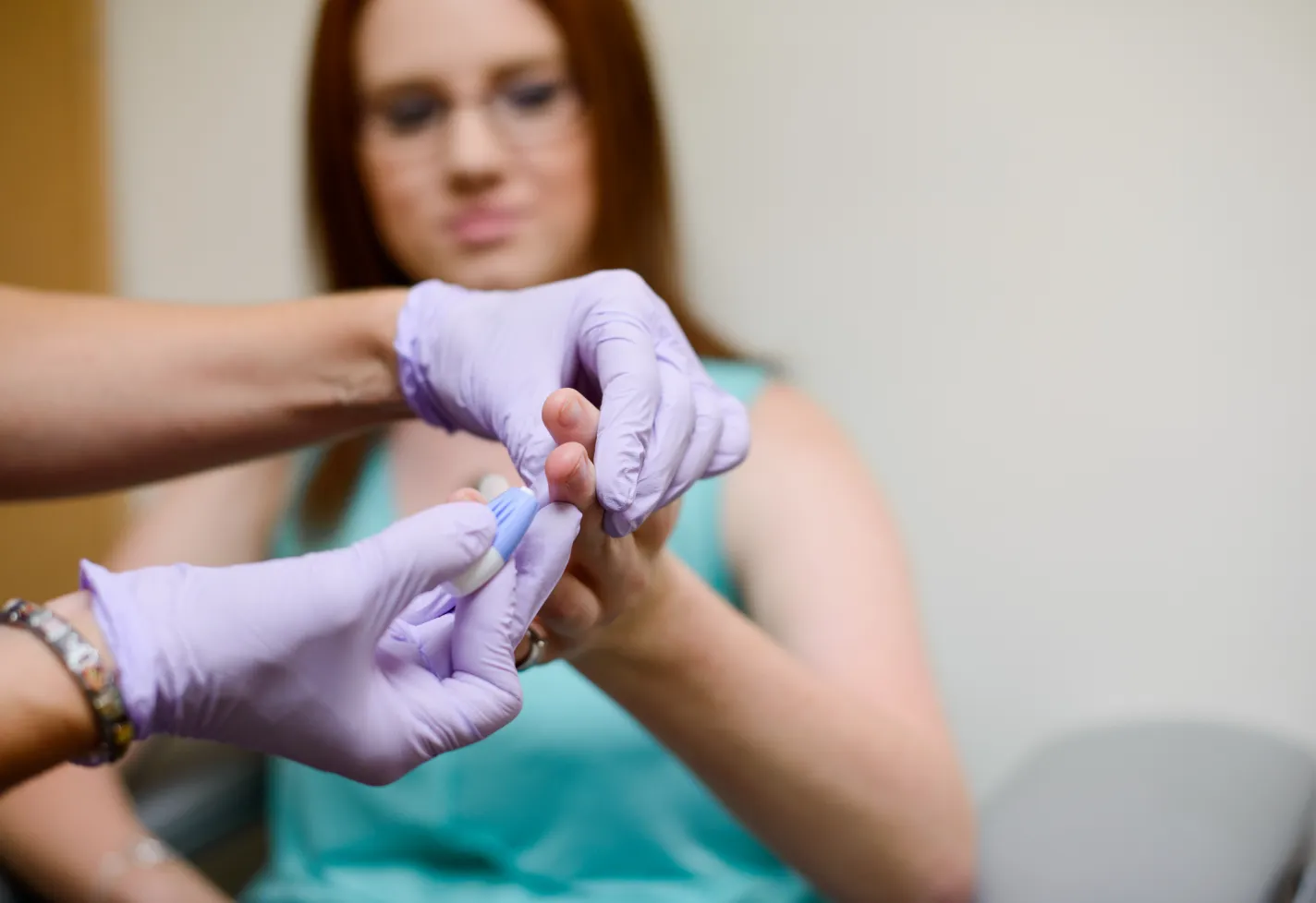A Novant Health nurse is holding a young woman's hand and finger in preparation for a blood test. 