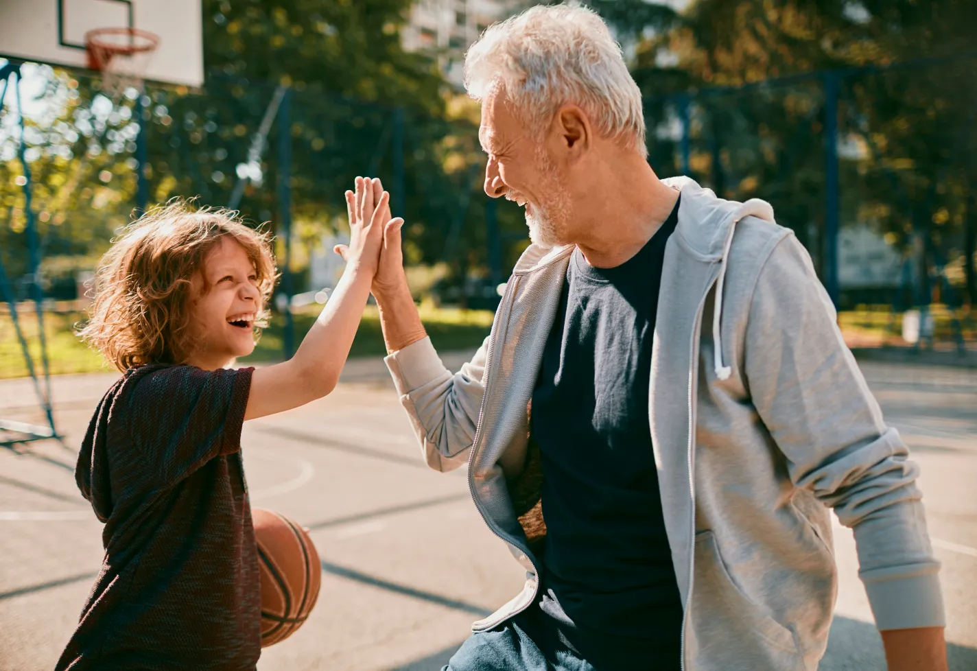 A young child is outside playing basketball with his grandfather. 