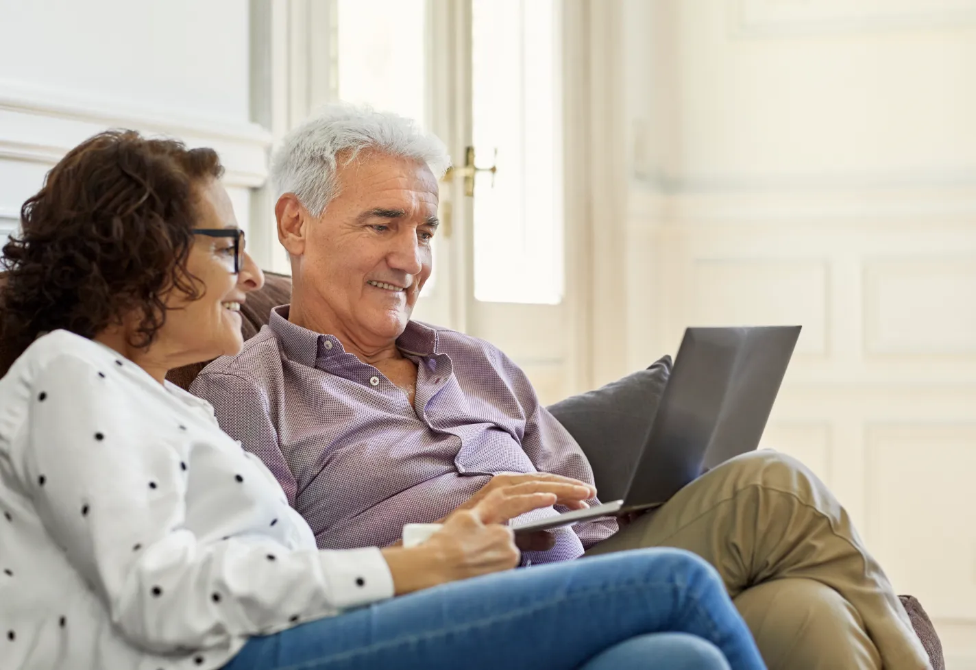 Senior couple sitting in their home reviewing information on a laptop. 