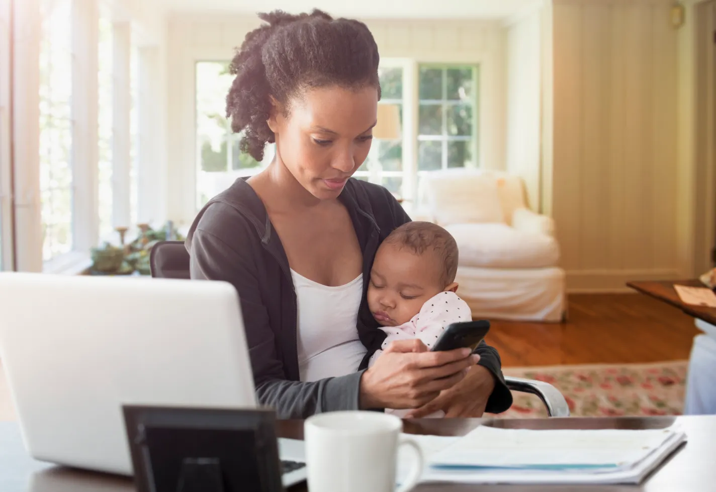 A mother is holding her baby as she sleeps while typing her phone. 