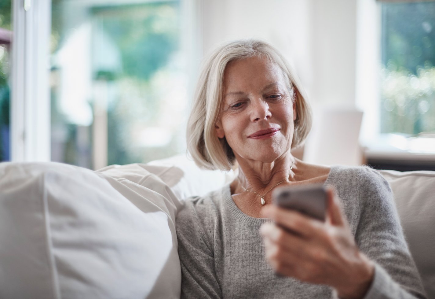 Senior woman sitting on a couch checking a smartphone