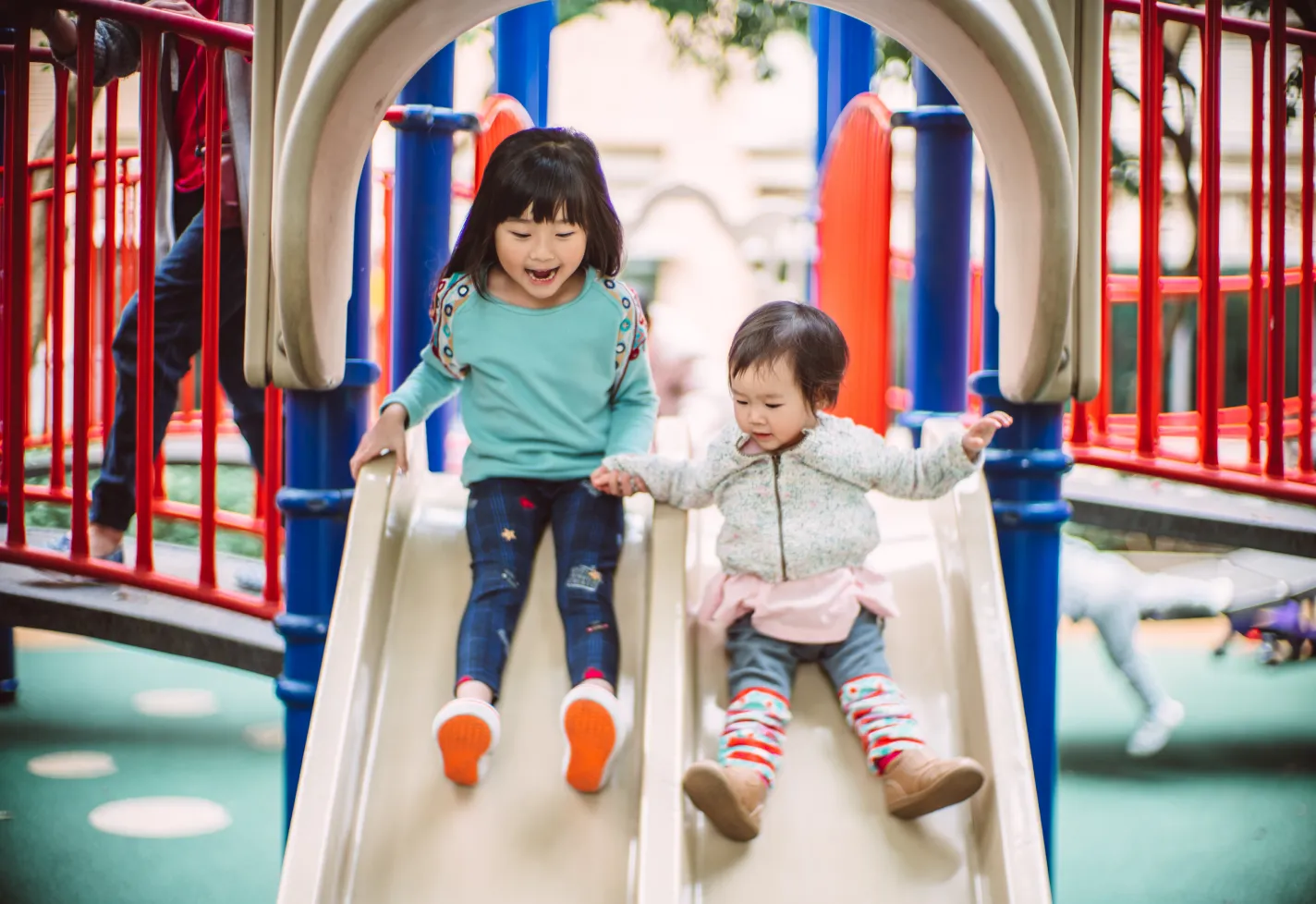 Two girls sliding down playground slide happily in the park