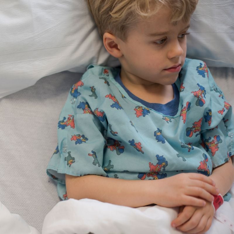 Young boy in a hospital gown sitting in a hospital bed. 