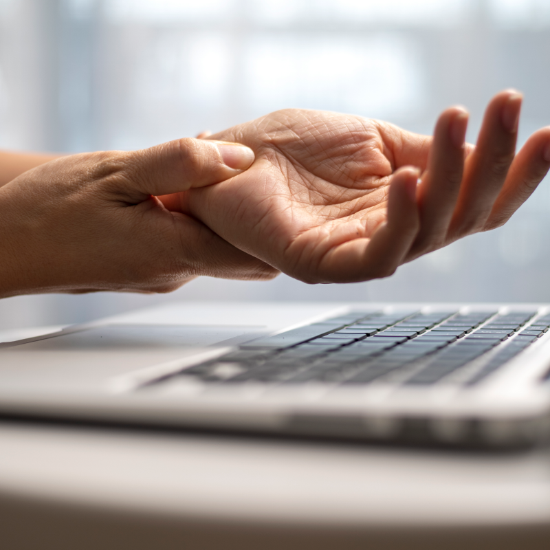 woman with carpal tunnel syndrome holding her hand near a laptop