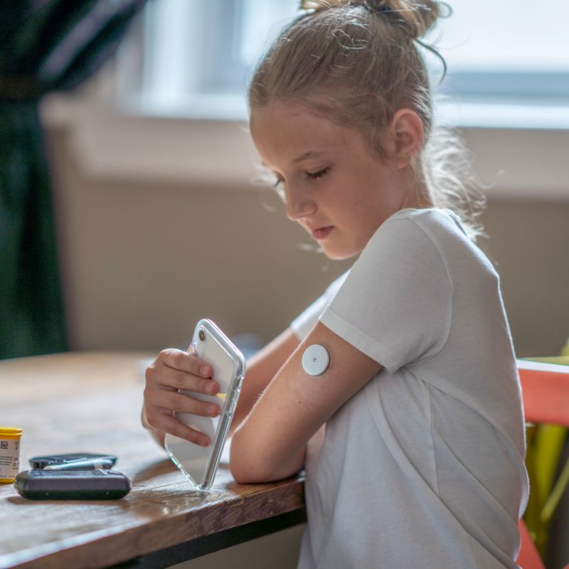 A young girl is using her phone to with her wearable diabetes device